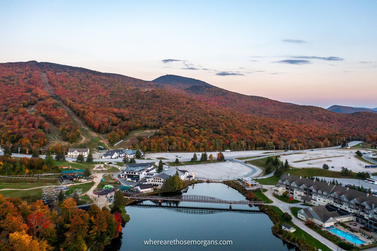 Drone photo overlooking Killington Mountain Resort in Vermont with a still lake and colorful leaves lighting up the mountains behind