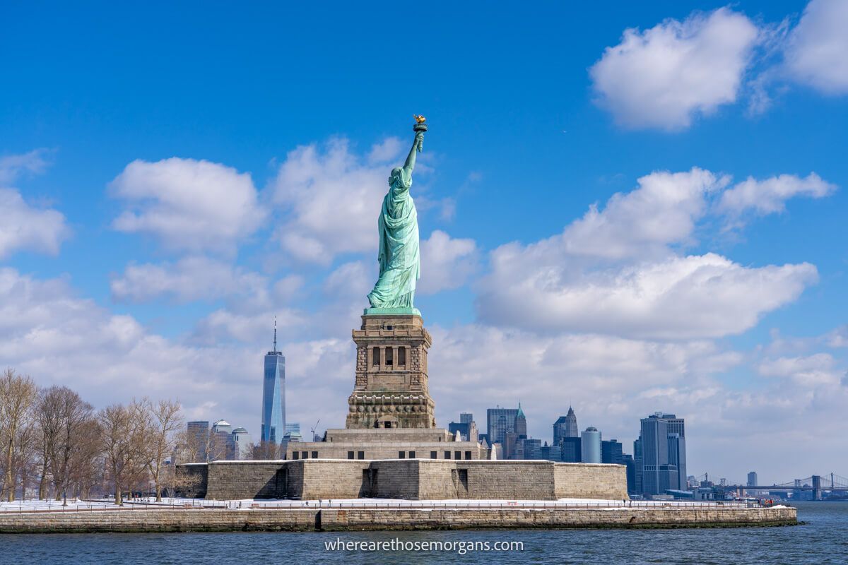 Photo of the back side of Lady Liberty with Lower Manhattan in the background on a clear sunny day