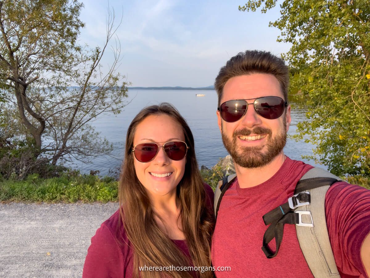 Couple wearing sunglasses and red shirts taking a selfie on a bike path with a lake behind