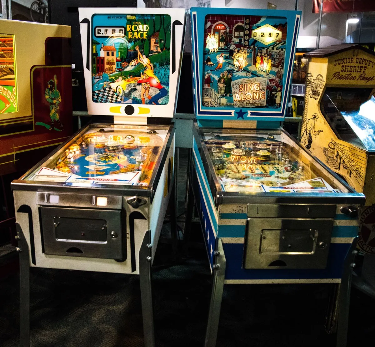Two pinball machines side by side in a dark room with dim lighting