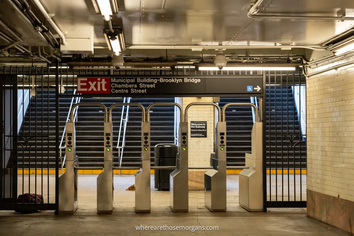 The inside of a subway station entrance with barriers and turnstyles but no people