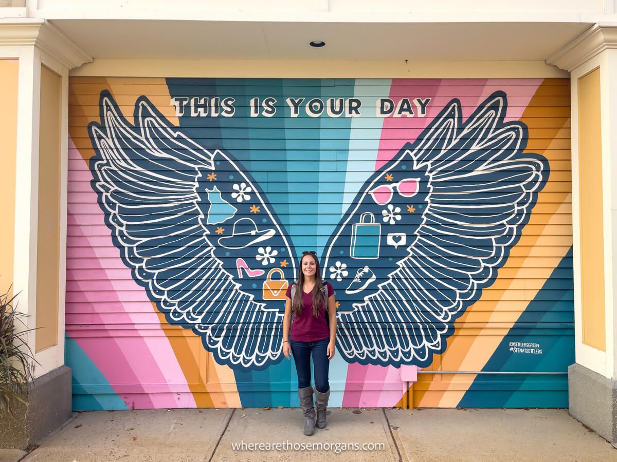 Tourist standing in the middle of large wings spray painted onto a wall. with lots of colors