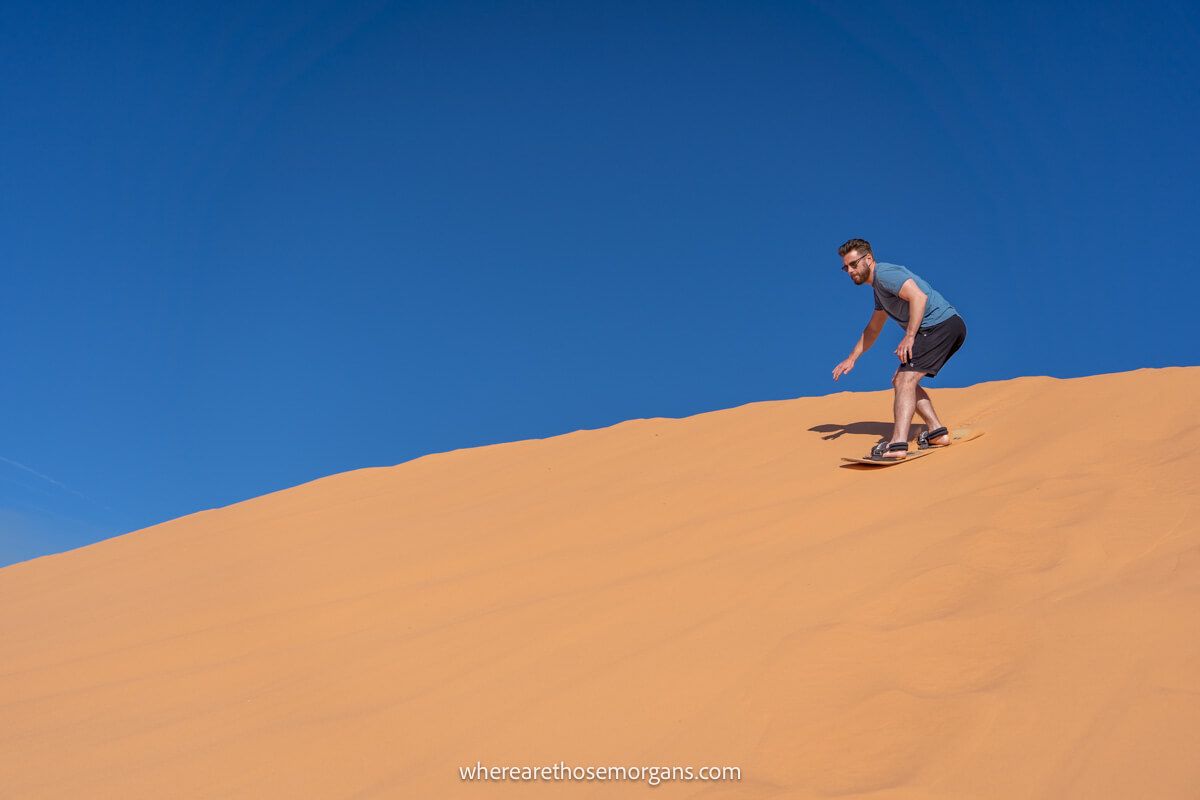 Sandboarder sliding down a tall sand dune on a clear day with brilliant blue sky