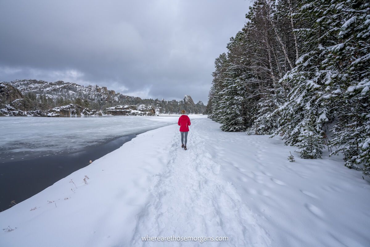 Hiker in red coat walking a snowy path around a lake