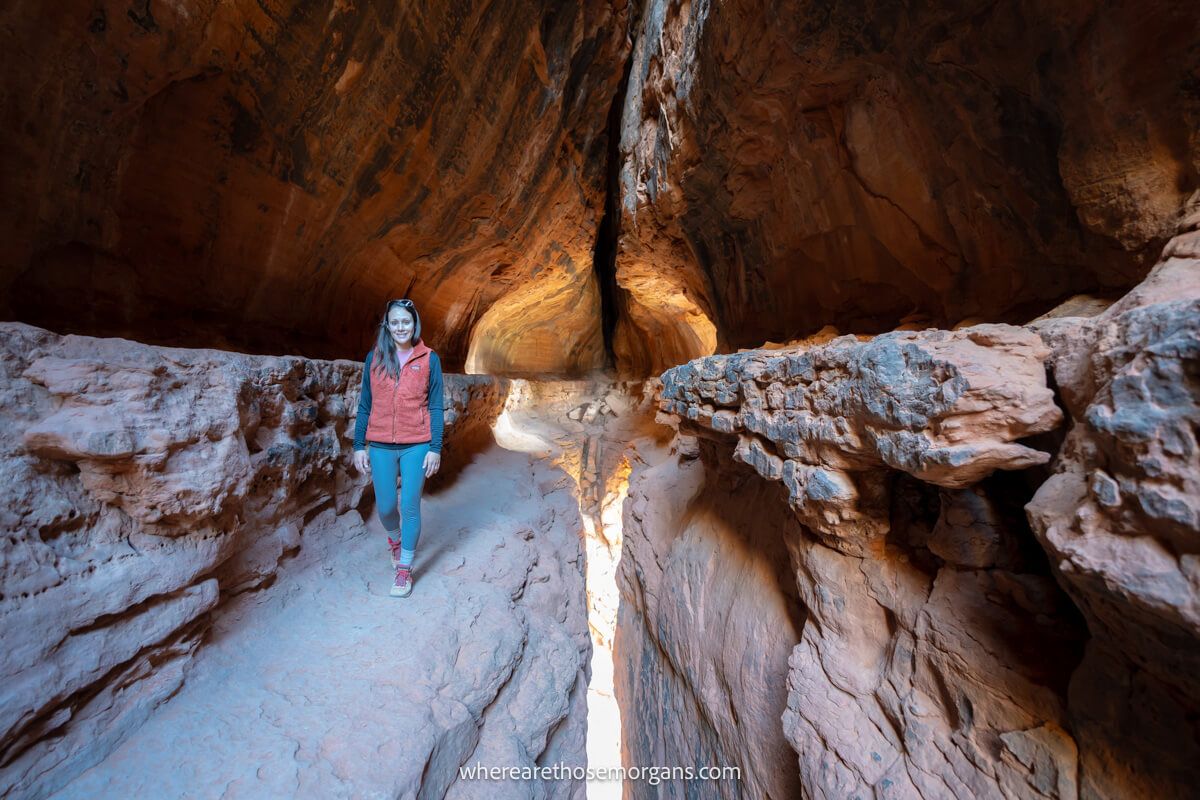 Hiker walking on a narrow ledge inside a tunnel like cave with light pouring in from below