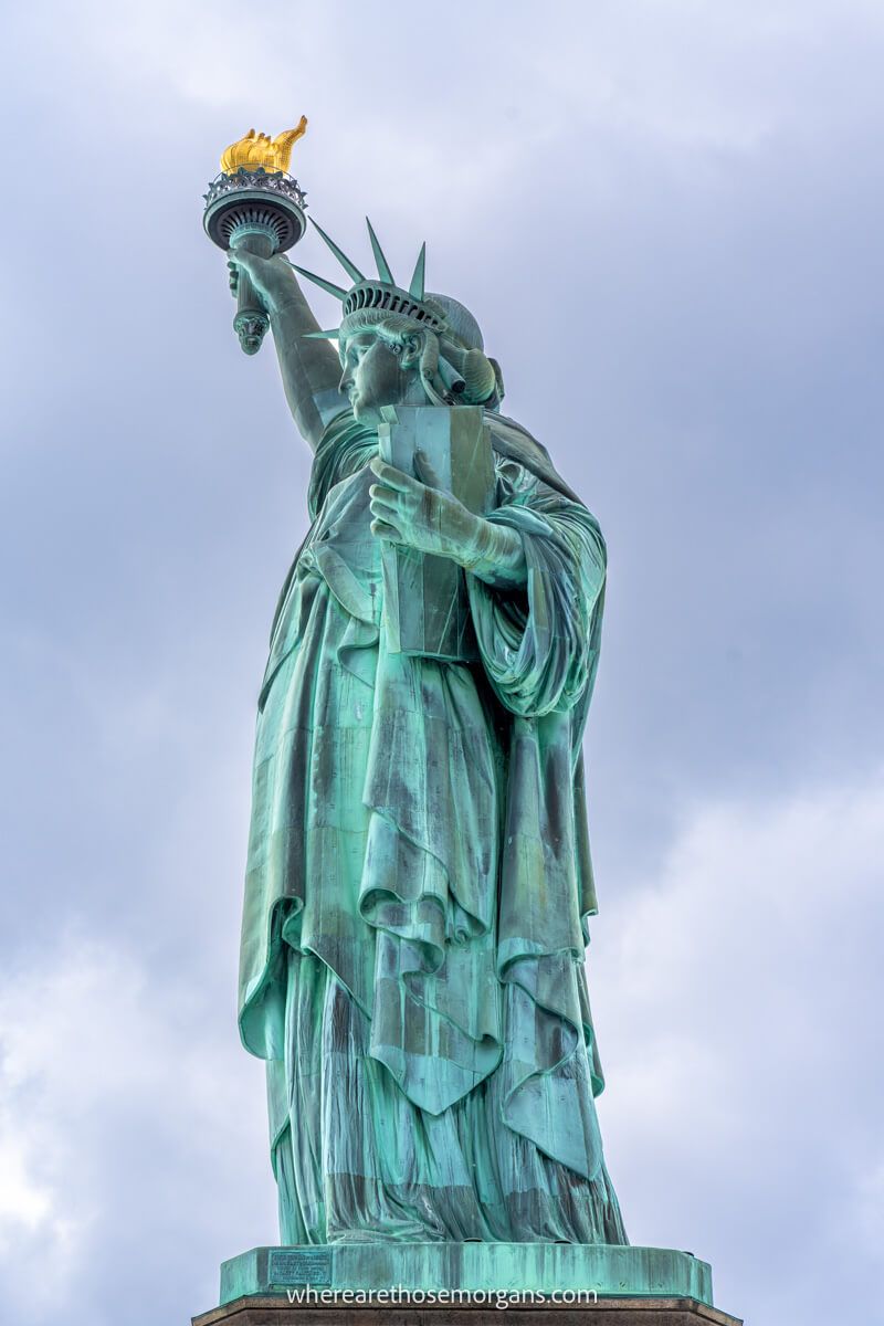 Photo close up on the side profile of the Statue of Liberty holding her torch aloft against a cloudy sky