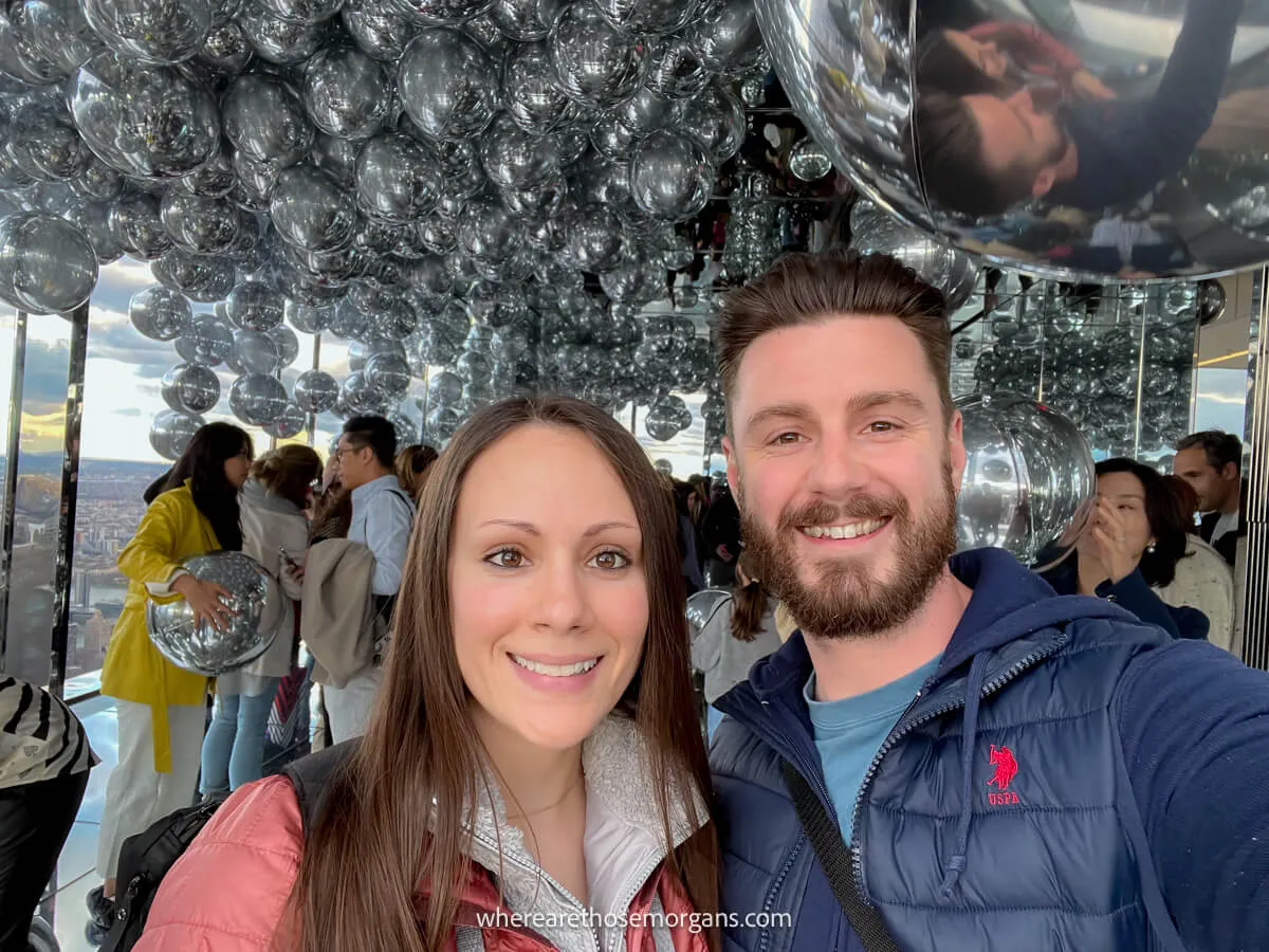 Close up photo of a couple taking a selfie inside a room filled with silver helium balloons