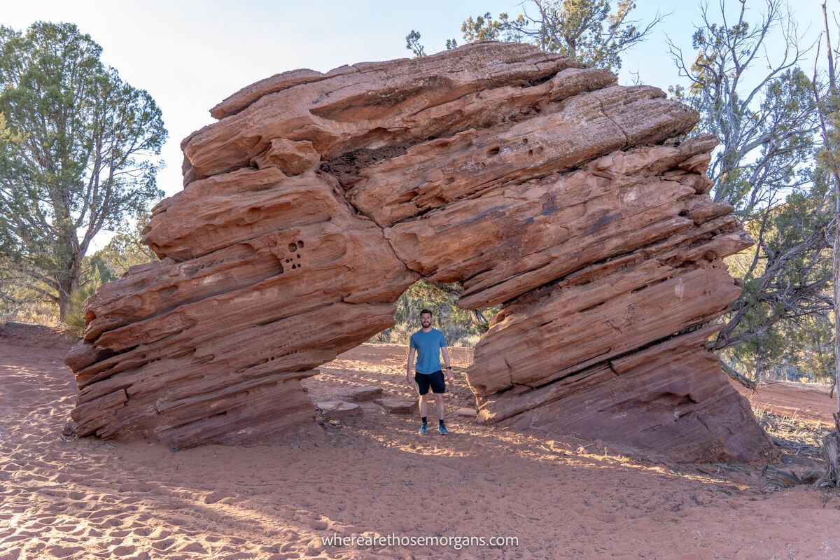 Hiker stood underneath a tall and thick natural sandstone arch on a sandy surface