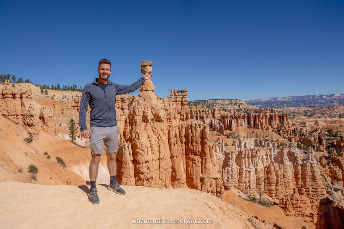 Hiker with arm in air pretending to grab a distant sandstone formation called Thor's Hammer in Bryce Canyon for a fun photo