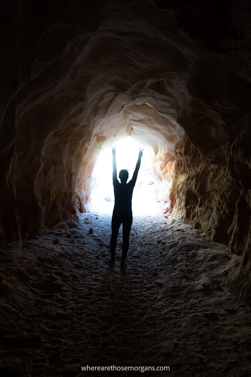 Photo of a hiker in a tunnel silhouetted with arms in the air and fingers sticking up at Belly of the Dragon Trail in Utah