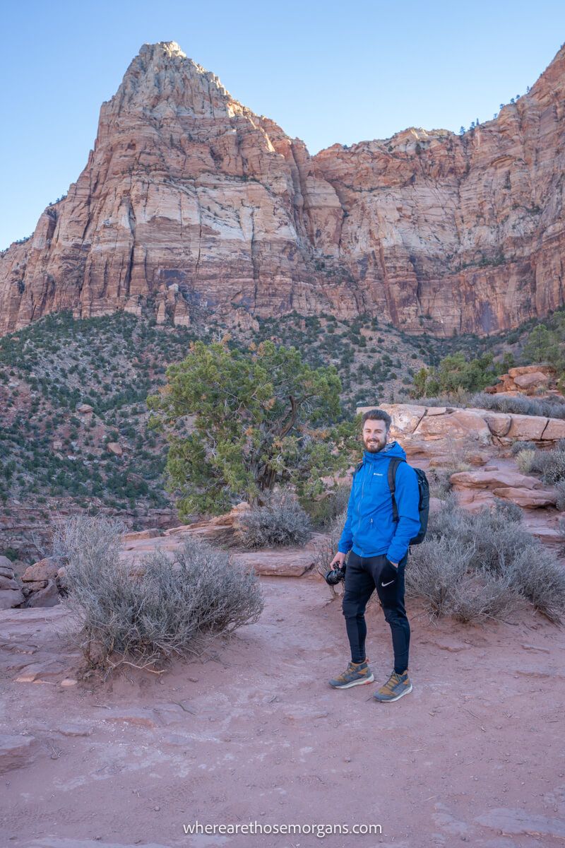 Photo of a hiker standing on red rocks in Zion with a coat on at sunrise in December