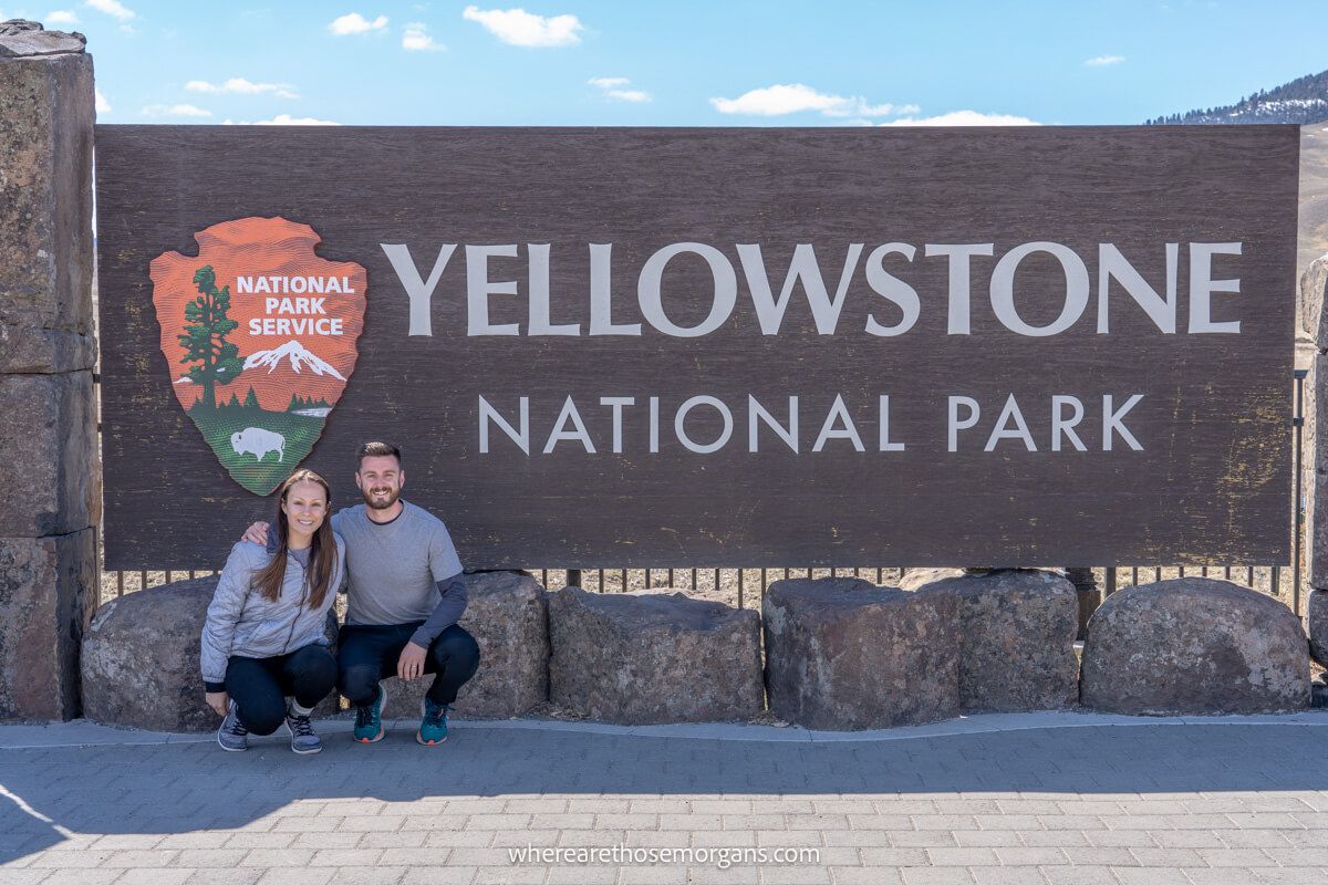 Couple kneeling down together for a photo with the Yellowstone National Park welcome sign in Montana